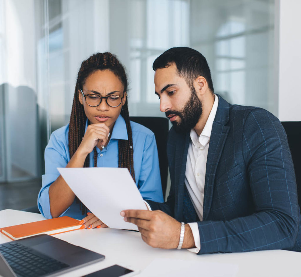 Puzzled male and female colleagues discussing information during cooperation briefing in office interior, multicultural partners in formal clothes analyzing paperwork reports and documents in company